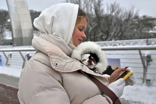 A woman looks at her smartphone as she keeps a dog in her jacket in Kyiv on November 22, 2023. (Photo by Sergei Supinsky/AFP Photo)