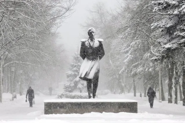 People walk past a monument to Russian poet Mikhail Lermontov during a major snowfall in the southern Russian city of Stavropol, on December 11, 2013. Snow fell today across Stavropol, while temperatures dropped to -10 C (14 F), but due to high humidity and wind, weather experts said it would feel more like -18 C (-1 F). (Photo by Danil Semyonov/AFP Photo)
