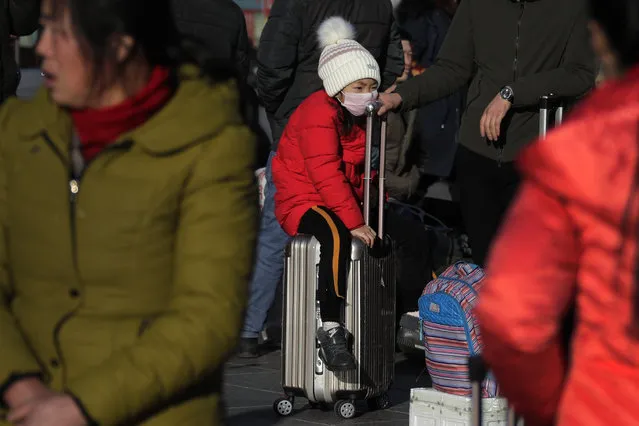 In this Wednesday, January 23, 2019, file photo, a child sits on a piece of luggage as she and others wait for their train at the Beijing railway station in Beijing. The world's largest annual migration began this week in China with millions of Chinese are traveling to their hometowns to celebrate the Lunar New Year on Feb. 5 this year which marks the Year of the pig on the Chinese zodiac. (Photo by Andy Wong/AP Photo)