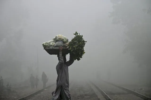 A worker carrying basket of vegetables, crosses railway tracks on a foggy winter morning in Lahore on December 28, 2023. (Photo by Arif Ali/AFP Photo)