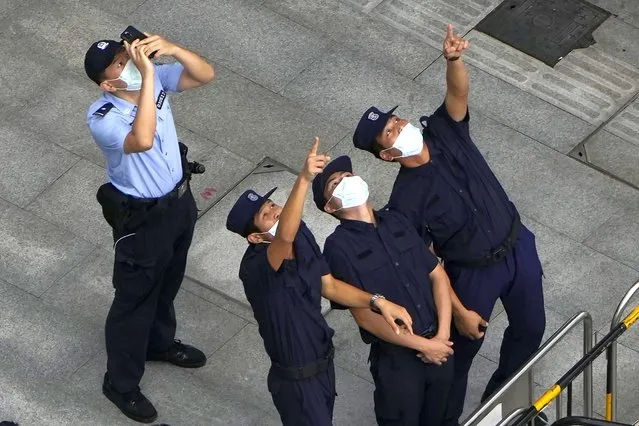 A police officer and security personnel react to something in the sky near the headquarters of the real estate developer Evergrande Group, Thursday, September 23, 2021, in Shenzhen, southern China. (Photo by Ng Han Guan/AP Photo)
