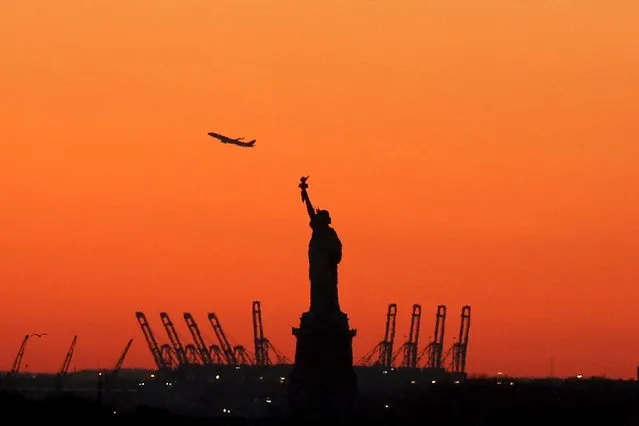 A plane is seen during take off in New Jersey behind the Statue of Liberty in New York's Harbor as seen from the Brooklyn borough of New York February 20, 2016. (Photo by Brendan McDermid/Reuters)