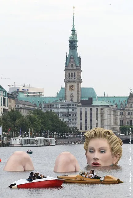 People in boats approach Die Badende (The Bather), a giant sculpture showing a woman's head and knees as if she were resting in the Binnenalster lake in Hamburg, Germany