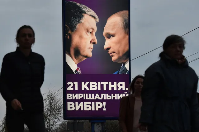People walk past a campaign poster with the current Ukrainian President Petro Poroshenko and Russian President Vladimir Putin (R) in Kiev on April 9, 2019, on the threshold of the second round of the presidential elections in Ukraine on Aprile 21. Ukraine's incumbent leader, 53-years-old, is eager to spar with his political novice rival, giving him a chance to show off his debating skills and outflank comedian Volodymyr Zelensky, 41-years-old, before a run-off vote on April 21. But he had to agree to a number of unusual conditions set down by, including a requirement for both of them to undergo medical tests to prove they do not abuse alcohol or drugs. (Photo by Vasily Maximov/AFP Photo)