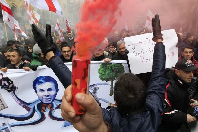 Protesters carry Georgian flags and a poster showing a caricature of former Prime Minister billionaire Bidzina Ivanishvili during a march in support of Rustavi 2 TV channel in Tbilisi, Georgia, Friday, February 10, 2017. Hundreds of people marched in central Tbilisi to express their support to independent TV channel Rustavi 2 and blamed the government and former Prime Minister Bidzina Ivanishvili for an attempt to silence opposition media. (Photo by Shakh Aivazov/AP Photo)