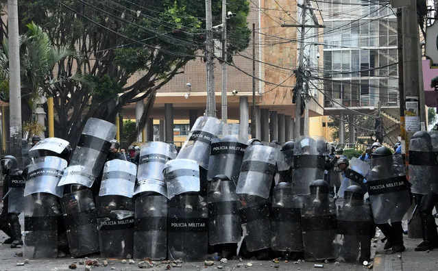 Honduran riot police take cover during clashes with students of the National Autonomous University of Honduras (UNAH) and elementary school teachers who protest against the approval of education and healthcare bills in the Honduran Congress in Tegucigalpa on April 29, 2019. Honduran police dispersed with teat gas thousands of people who protested and blocked roads against education and healthcare reforms approved by the Congress. (Photo by Orlando Sierra/AFP Photo)