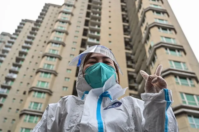 A worker wearing protective gear gestures as people wait to be tested for the Covid-19 coronavirus at a residential compound in Shanghai on March 18, 2022. (Photo by Hector Retamal/AFP Photo)