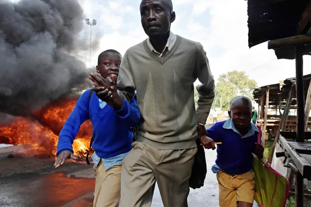 A man leads school children away from teargas and a burning barricade in Kibera slum, Nairobi on May 23, 2016 during a demonstration of opposition supporters demanding a change of leadership at the electoral commission ahead of a vote due next year. (Photo by Carl De Souza/AFP Photo)