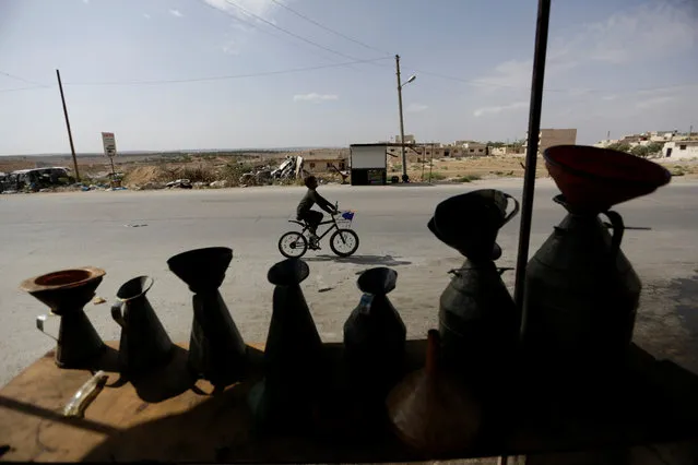 A boy rides a bicycle near displayed containers in a petrol shop, in the rebel-controlled area of Maaret al-Numan town in Idlib province, Syria May 26, 2016. (Photo by Khalil Ashawi/Reuters)