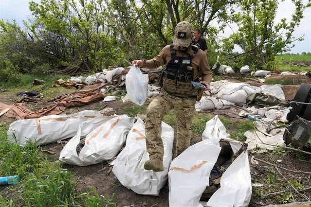 A Ukrainian serviceman works during the exhumation of killed Russian soldiers' at their former positions near the village of Malaya Rohan, on the outskirts of Kharkiv, Wednesday May 18, 2022. (Photo by Andrii Marienko/AP Photo)
