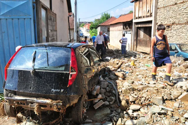 People pass beside destroyed cars walking over mud, rocks and debris piled after a flood in the village of Golema Recica, just near the town of Tetovo, in northwestern Macedonia, on Tuesday, August 4, 2015. (Photo by Zoran Andonov/AP Photo)