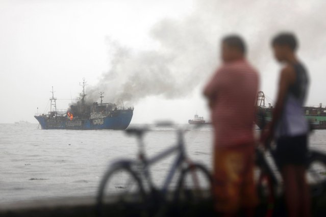 Locals look on as smoke rises from a burning ship that ran aground in Manila Bay, Philippines, 02 September 2024. At least four ships moored inside the Manila Bay were run aground after being hit by strong waves brought by Tropical Storm Yagi. In a report by the National Disaster Risk Reduction and Management (NDRRMC) on September 02, two people died and scores were injured by Tropical Storm Yagi. The state weather agency of the Philippines warned residents living along the typhoon's path to take precautionary measures due to possible flash floods in low-lying areas and landslides in mountainous villages. (Photo by Francis R Malasig/EPA/EFE)