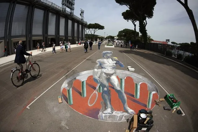 People pass by a painting showing a Roman statue holding a tennis racket on the day of the quarter-finals match of the ATP and WTA Rome tournament on May 18, 2012