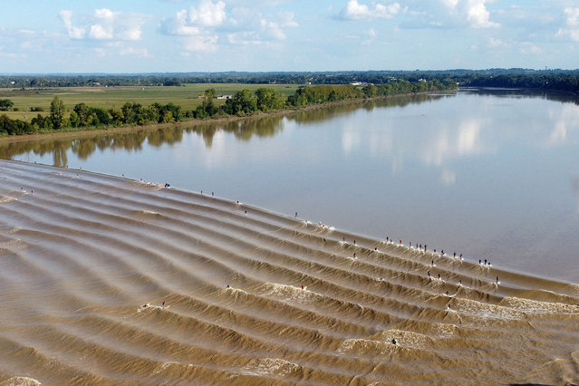 This aerial picture shows surfers riding the Mascaret wave up the Dordogne river to the port of Saint Pardon, south-western France, on September 18, 2024. The Mascaret is a tidal phenomenon in which the leading edge of the incoming tide forms a wave of water that travels up a river or narrow bay. (Photo by Romain Perrocheau/AFP Photo)