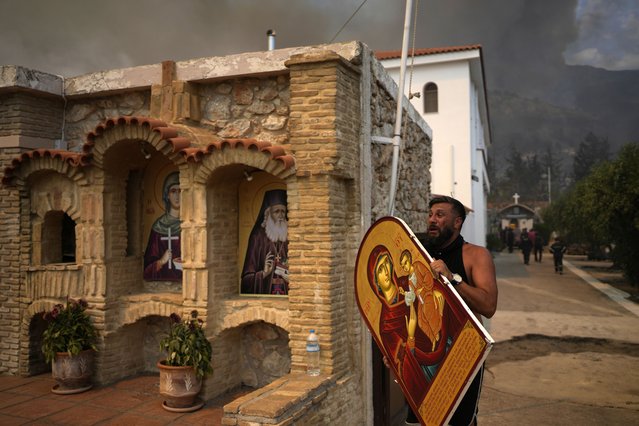 A man carries a saint Mary with Jesus icon to save it from a wildfire at Agia Paraskevi Christian Orthodox monastery in Acharnes a suburb of northern Athens, Greece, Wednesday, August 23, 2023. Water-dropping planes from several European countries joined hundreds of firefighters Wednesday battling wildfires raging for days across Greece that have left 20 people dead, while major blazes were also burning in Spain's Tenerife and in northwestern Turkey near the Greek border. (Photo by Thanassis Stavrakis/AP Photo)