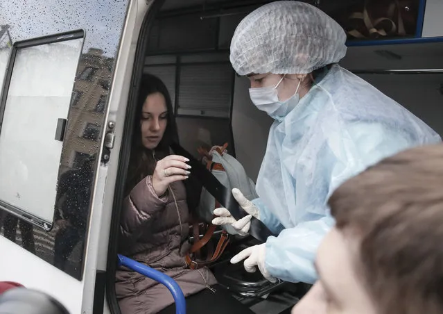 An emergency medic helps Alla Ilyina, who broke out of the hospital on Feb. 7 after learning that she would have to spend 14 days in isolation instead of the 24 hours doctors promised her, to fasten a seat belt inside an ambulance after a court session in St.Petersburg, Russia, Monday, February 17, 2020. A woman who escaped from a hospital in St. Petersburg, where she was being kept in isolation for possible inflection by the new coronavirus, was ordered by court on Monday to return back to the quarantine for at least two days. (Photo by Dmitri Lovetsky/AP Photo)