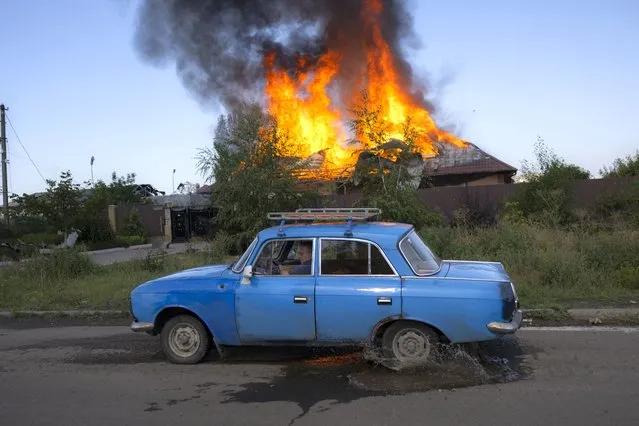 A Ukrainien man drives past a burning house hit by a shell in the outskirts of Bakhmut, Eastern Ukraine, on July 27, 2022, amid the Russian invasion of Ukraine. (Photo by Bulent Kilic/AFP Photo)