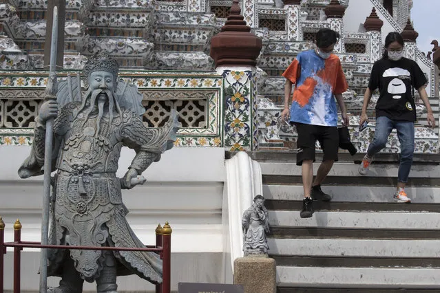 Tourists wearing protective masks walk down the steps at Temple of Dawn in Bangkok, Thailand, Thursday, March 12, 2020. For most people, the new coronavirus causes only mild or moderate symptoms. For some it can cause more severe illness. (Photo by Sakchai Lalit/AP Photo)