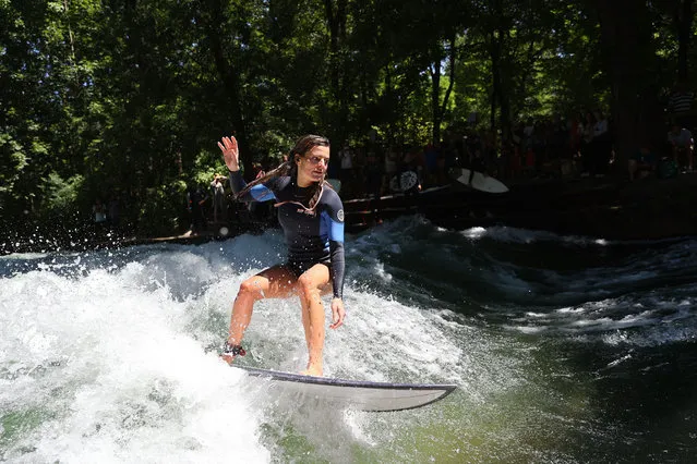 A surfer rides her surfboard on the wave at Eisbach which is an artificial river and also flows for a long stretch through the English Garden (Englischer Garten) in Munich, Germany on July 17, 2022. The river is a hot spot for surfers. Artificial surf waves at two different points, offer surfers the opportunity to surf according to their experience. (Photo by Gokhan Balci/Anadolu Agency via Getty Images)