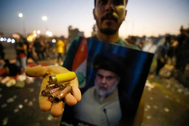 A supporter of Iraqi Shiite cleric Moqtada Sadr carries bullet casings and a spent shotgun shell in the capital Baghdad's Green Zone, on August 29, 2022. Dozens of angry supporters of the powerful cleric stormed the Republican Palace, a ceremonial building in the fortified Green Zone, a security source said, shortly after Sadr said he was quitting politics. The army has announced a  Baghdad-wide curfew to start from 3:30 pm (1230 GMT). (Photo by Ahmad Al-rubaye/AFP Photo)