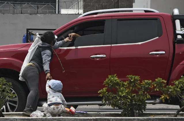 A woman holding her child and a white flag as a signal that they need food, receives alms from a driver at a highway in Villa Nueva, 15 km south Guatemala City on May 6, 2020, amid the new coronavirus pandemic. Guatemalan President Alejando Giammattei extended until May 11 the partial curfew imposed against the COVID-19 pandemic, which has killed 19 out of 763 reported cases. (Photo by Johan Ordonez/AFP Photo)