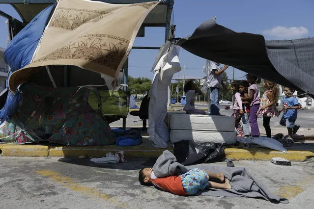 Children play as another one lies on a blanket at the old international airport, which is used as a shelter for over 2,800 refugees and migrants, in southern Athens, on Thursday, August 4, 2016. Daily arrivals by migrants and refugees at Greek islands near the Turkish coast have remained low since the July 15 coup attempt, but about 57,000 people remain stranded in Greece, most in army-built camps on the mainland. (Photo by Thanassis Stavrakis/AP Photo)