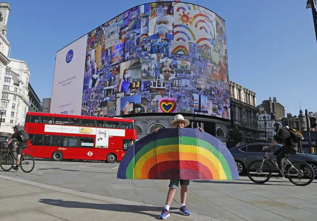 A young boy holds a painted rainbow as pictures appear on a screen during a 10 minute domination on The Piccadilly Lights, Piccadilly Circus, to mark the launch of The People's Picture interactive mosaic art project Rainbows for the NHS in London, Monday, June 22, 2020. The art installation which features thousands of photos and messages from key workers, carers, patients, doctors and nurses appears on Piccadilly Lights until June 28. (Photo by Frank Augstein/AP Photo)