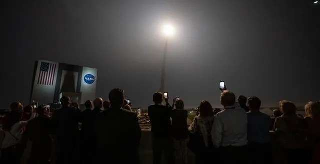 In this handout photo provided by NASA on November 16, 2022, people watch as the Artemis I unmanned lunar rocket lifts off from launch pad 39B at NASA's Kennedy Space Center in Cape Canaveral, Florida. NASA's Artemis 1 mission is a 25-and-a-half day voyage beyond the far side of the Moon and back. The meticulously choreographed uncrewed flight should yield spectacular images as well as valuable scientific data. (Photo by Bill Ingalls/NASA via AFP Photo)