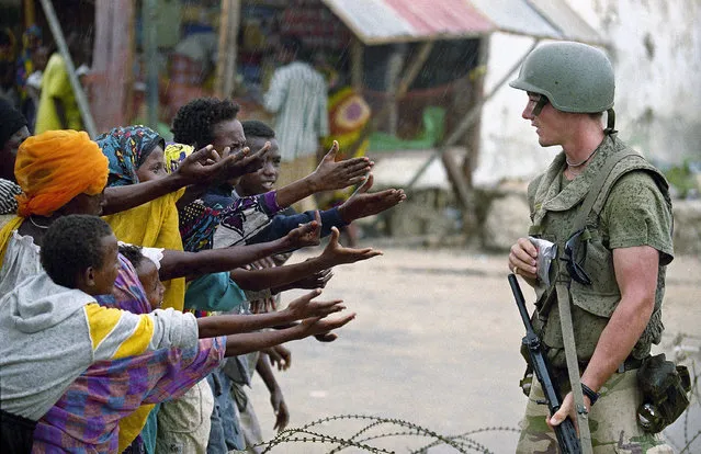 Somali children reach begging an Italian U.N. soldier for some candy at a checkpoint in Mogadishu, June 23, 1993. While U.N. soldiers hunt for him, warlord Mohamed Farrah Aidid is talking to reporters, declaring his innocence in the deaths of Pakistani Peacekeepers. (Photo by Hansi Krauss/AP Photo)
