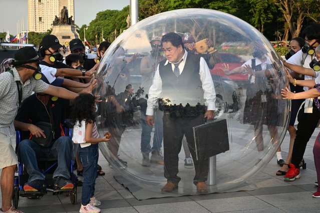 Philippine actor Soliman Cruz wearing a business suit stands inside an 8-foot transparent bubble while other activists wearing masks touch the bubble during an anti-pollution protest near a park in Manila on April 25, 2025. The protest is part of a climate advocates 350 campaign on Manila's air pollution crisis, due to traffic emissions, fossil fuel and unchecked industrial activity. (Photo by Ted Aljibe/AFP Photo)