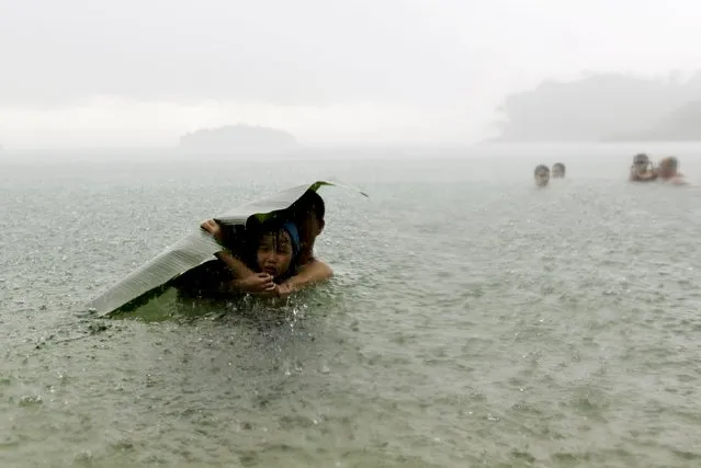 A young girl covers herself from the rain with a banana leaf next to a man in the sea on the outskirts of Colon City October 17, 2015. (Photo by Carlos Jasso/Reuters)