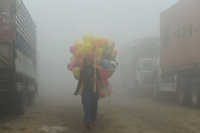 A Pakistani vendor carries baloons on a street amid heavy smog in Lahore on November 9, 2017. Flights were cancelled, school times pushed back and hospitals flooded as air pollution inundated Pakistan's second largest city Lahore November 8. The fast-developing country suffers from some of the worst air pollution in the world, thanks to its giant population navigating poorly maintained vehicles on its roads and unchecked industrial emissions along with seasonal crop burning. (Photo by Arif Ali/AFP Photo)