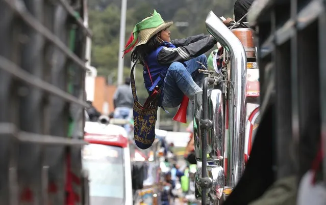 An Indigenous youth climbs the side of a bus during a national strike in Bogota, Colombia, Wednesday, October 21, 2020. (Photo by Fernando Vergara/AP Photo)