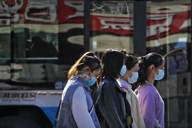 Women wearing face masks to help curb the spread of the coronavirus walk along a moving bus on a street in Beijing, Wednesday, October 28, 2020. (Photo by Andy Wong/AP Photo)