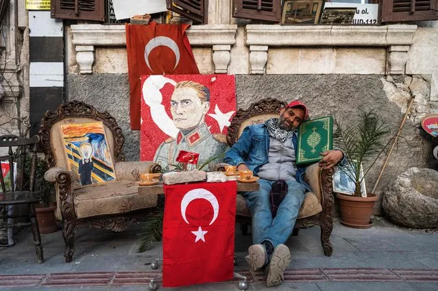 Serkan Sincan, 51, poses with a Qoran found in the rubble of a collapsed building next to a portrait of modern Turkey founder Mustafa Kemal Ataturk in front of his antique shop in the historic part of Antakya on March 7, 2023. While the residents of the city still mourn the huge loss of human lives and memories amid apocalyptic scenes of devastation, Serkan Sincan keeps his shop open in the abandoned street since the third day of the massive 7.8 magnitude quake on February 6. (Photo by Ozan Kose/AFP Photo)