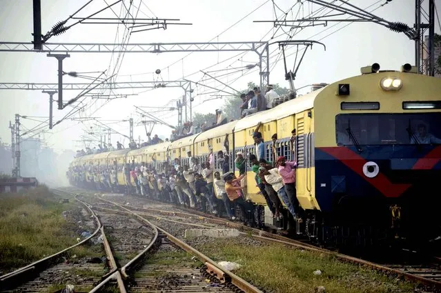 Indian passengers hang from the doors of the coaches of an over crowded train to travel home for the Chhath Puja festival dedicated to the Sun God, at Parsa Bazar railway station in Patna, Bihar state, India, Monday, November 16, 2015. People travel home from Bihar in large numbers for Chhath, one of the most significant festival for people in the region. (Photo by Aftab Alam Siddiqui/AP Photo)