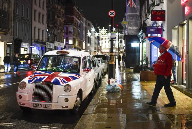 A taxi driver holds a Union flag themed umbrella as he walks towards his Union flag themed taxi in Mayfair, ahead of the new Tier-4 restriction measures, in London, Saturday, December 19, 2020. Britain's Prime Minister Boris Johnson says Christmas gatherings cannot go ahead and non-essential shops must close in London and much of southern England as he imposed a new, higher level of coronavirus restrictions to curb rapidly spreading infections. (Photo by Alberto Pezzali/AP Photo)