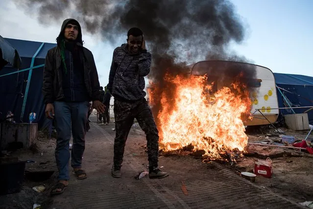 Migrants walk next to a fire caused by other migrants setting alight some of their belongings, as workers dismantle the makeshift camp “the Jungle” during its evacuation in Calais, France, 25 October 2016. The camp that held more than 7,000 migrants started being dismantled on 24 October, a process that shall take a week according tho the French authorities. (Photo by Etienne Laurent/EPA)