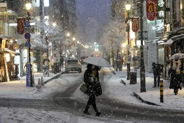 People walk along a shopping street as the snow comes down, January 6, 2022, in Tokyo. The risk of typhoons in Japan has gone up and the amount of snowfall has declined, even as the threat of heavy snowfall remains. (Photo by Kiichiro Sato/AP Photo)