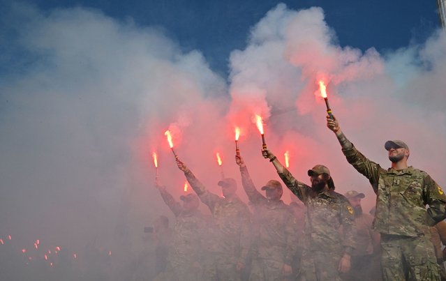 Ukrainian servicemen burn flares during a memorial event at Independence Square in Kyiv, Ukraine, on Saturday, July 29, 2024. Two years ago, more than 50 Ukrainian prisoners of war were killed in an attack on the Olenivka detention center near Donetsk. (Photo by Sergei Supinsky/AFP Photo)