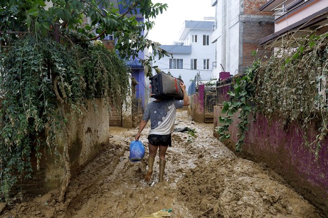 A man walks on a muddy alleyway carrying belongings salvaged from his house in Kathmandu, Nepal, Monday, September 30, 2024 in the aftermath of a flood caused by heavy rains. (Photo by Gopen Rai/AP Photo)