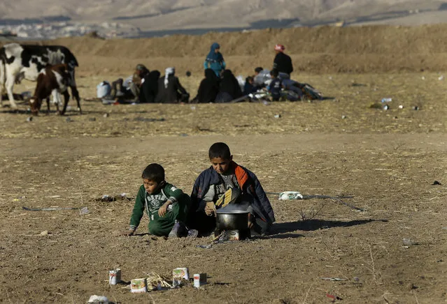 Iraqi boys who fled with their parents the fighting between Iraqi forces and Islamic State militants, cook as they wait to cross to the Kurdish controlled area, in an open field in the Nineveh plain, northeast of Mosul, Iraq, Friday November 18, 2016. (Photo by Hussein Malla/AP Photo)