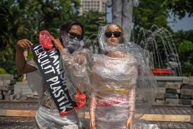 An environmental activist wearing plastic next to mannequins dressed in plastic waste takes part in a campaign against climate change to mark the World Environment Day in Surabaya, Indonesia on June 6, 2023. (Photo by Juni Kriswanto/AFP Photo)