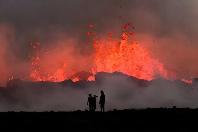 People watch flowing lava during an volcanic eruption near Litli Hrutur, south-west of Reykjavik in Iceland on July 10, 2023. A volcanic eruption started on July 10, 2023 around 30 kilometres (19 miles) from Iceland's capital Reykjavik, the country's meteorological office said, marking the third time in two years that lava has gushed out in the area. “The eruption is taking place in a small depression just north of Litli Hrutur, from which smoke is escaping in a north-westerly direction”, the office said. Footage circulating in the local media shows a massive cloud of smoke rising from the ground as well as a substantial flow of lava. (Photo by Kristinn Magnusson/AFP Photo)