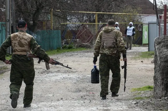 Pro-Russian separatists walk in a street patrolled by OSCE observers in the village of Shyrokyne, eastern Ukraine, Thursday, April 16, 2015. Shyrokyne, a village on the Azov Sea that has been the epicenter of recent fighting, has changed hands repeatedly throughout the conflict.  (AP Photo/Evgeniy Maloletka)