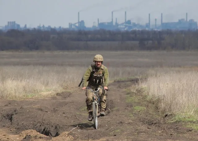 A service member of the Ukrainian armed forces rides a bicycle at fighting positions on the line of separation near the rebel-controlled city of Donetsk, as the Avdiivka Coke Plant seen in the background, near Donetsk, Ukraine on April 17, 2021. (Photo by Serhiy Takhmazov/Reuters)