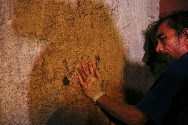 A funeral parlour worker, his hands bloodied from carrying bodies, rests against the wall of a house in Manila, Philippines early November 1, 2016. According to police and witnesses, unknown masked gunmen killed five people inside the house that is a known drug den. (Photo by Damir Sagolj/Reuters)