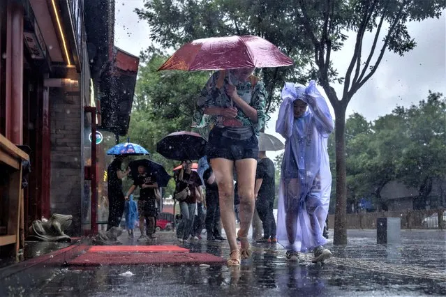 People wear raincoats and shelter under umbrellas in a tourist area during heavy rain in Beijing, China on July 30, 2023. (Photo by Thomas Peter/Reuters)
