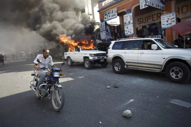 A man riding a bike passes next to a car that was set afire by protesters during a demonstration against the electoral process in Port-au-Prince, Haiti, January 18, 2016. Haiti's delayed presidential run-off election will take place on January 24. (Photo by Andres Martinez Casares/Reuters)