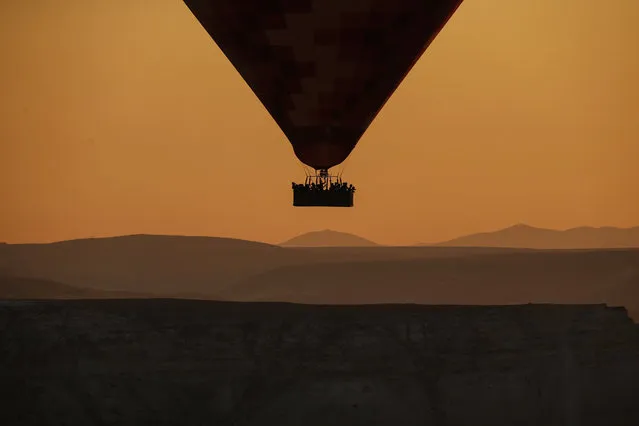 A hot air balloon, carrying tourists, rises into the sky at sunrise in Cappadocia, central Turkey, early Tuesday, August 7, 2018.  Cappadocia has become a favourite site for tourists in hot-air balloons who can slowly drift above the cone-shaped rock formations and then float up over rippled ravines for breathtaking views over the region. (Photo by Emrah Gurel/AP Photo)